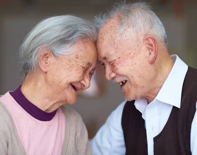 A happy older couple smiling as they lean foreheads on each other.