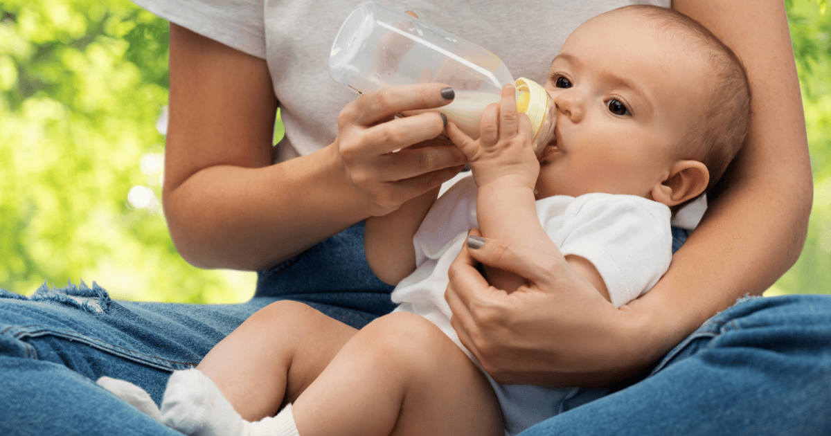 Mother feeding her baby a bottle of formula while looking tired and uncertain, highlighting the emotional complexity of infant feeding decisions.