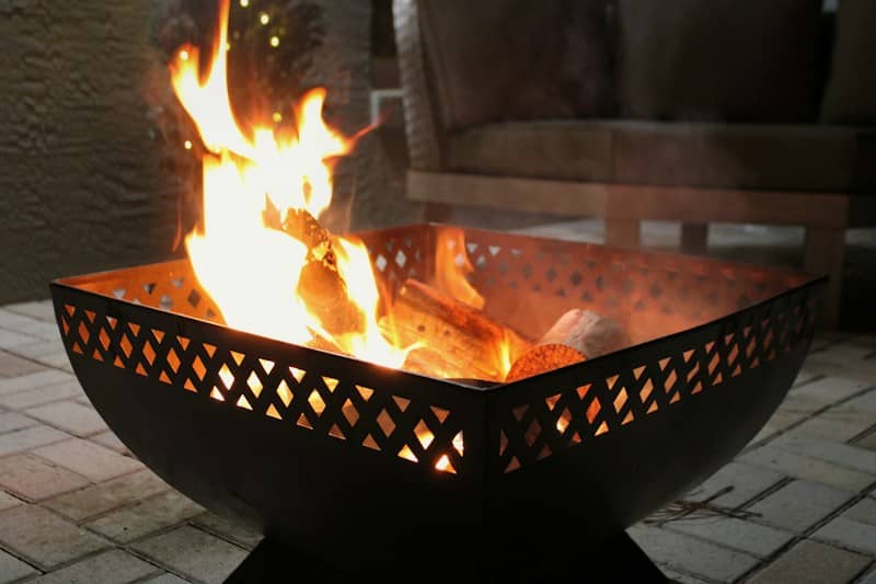 A bright fire burning in a black metal fire pit on a patio
