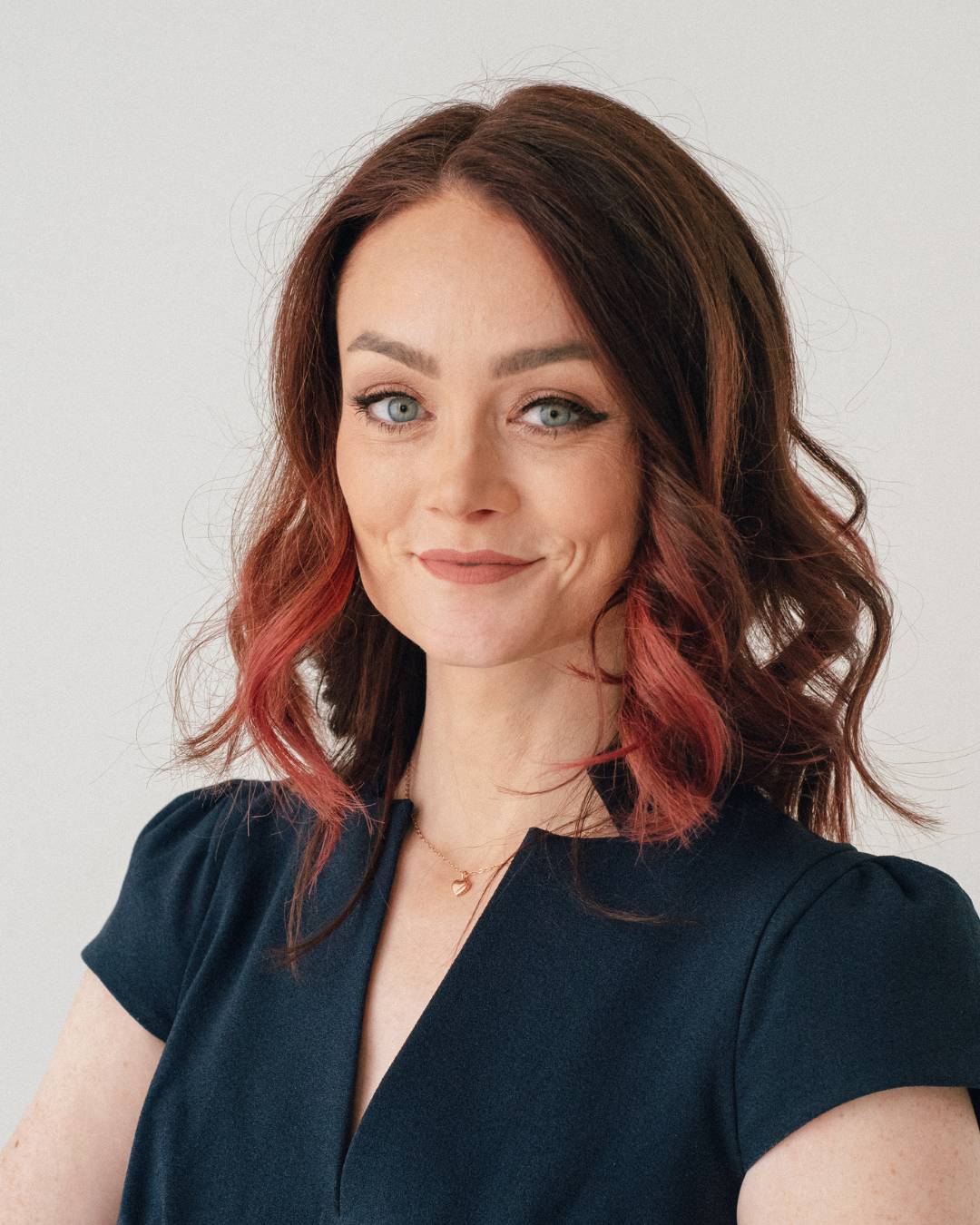 A photo of Kristin. She has shoulder-length auburn hair, pale skin, and blue eyes; and she's wearing a navy blue blouse. Her expression is a slight, knowing smile.
