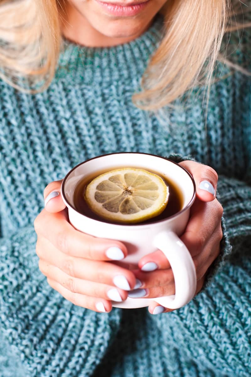 A woman holding a cup of tea with a lemon slice in it