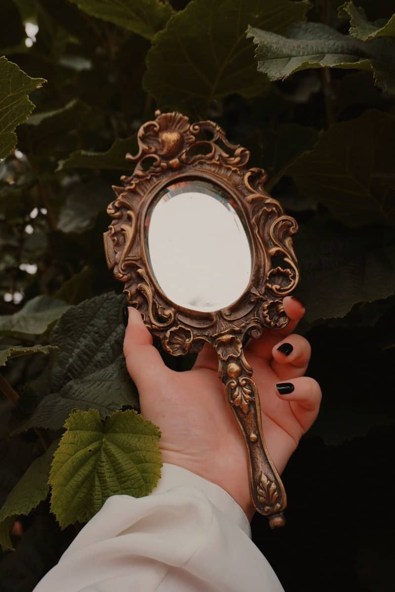 Hand holding ornate antique hand mirror with foliage.