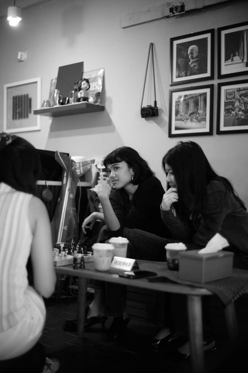 Three people sitting at a table with a chessboard and drinks in a cafe