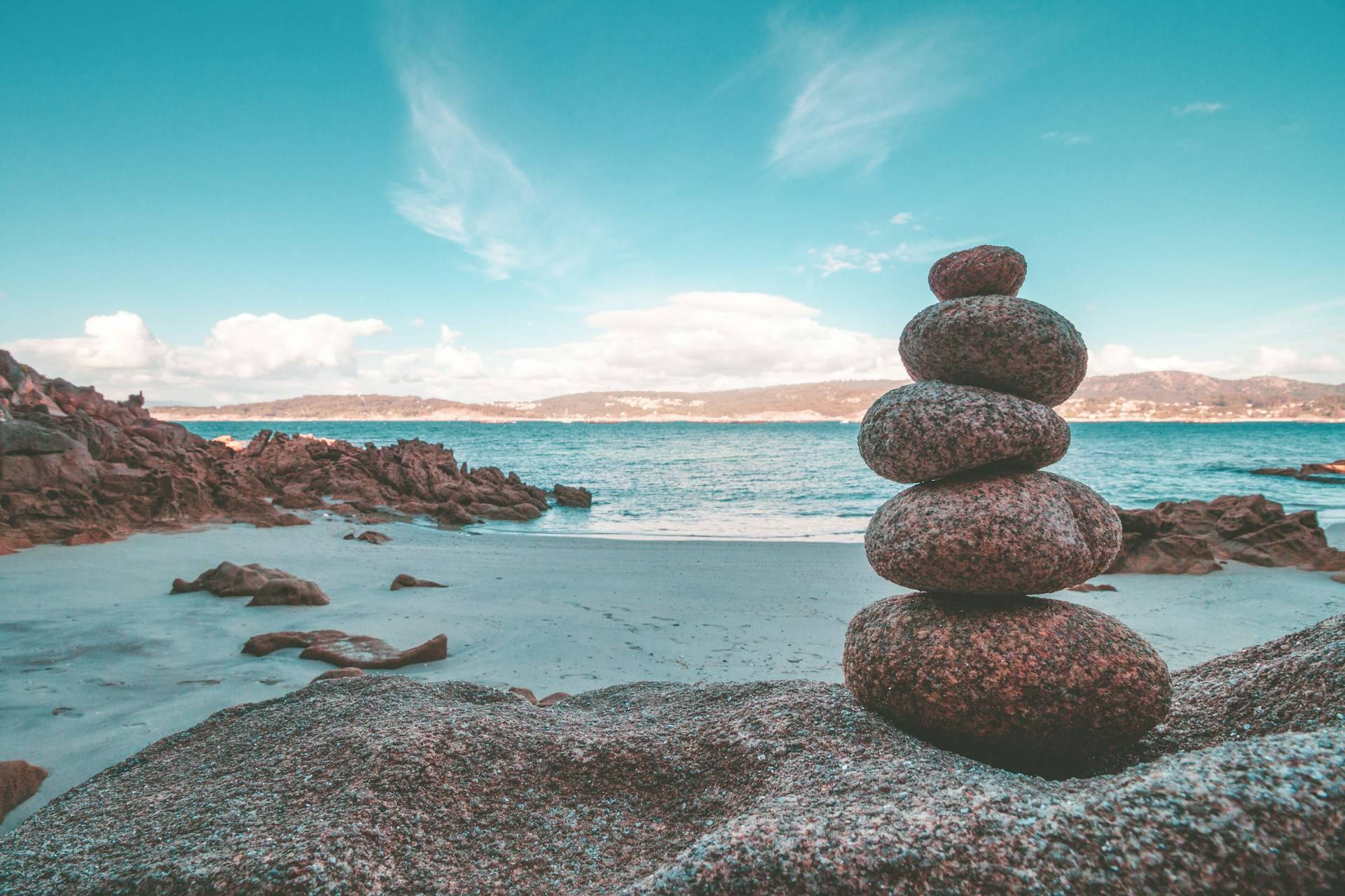 A peaceful coastal landscape featuring a stack of balanced rocks overlooking a calm sea.