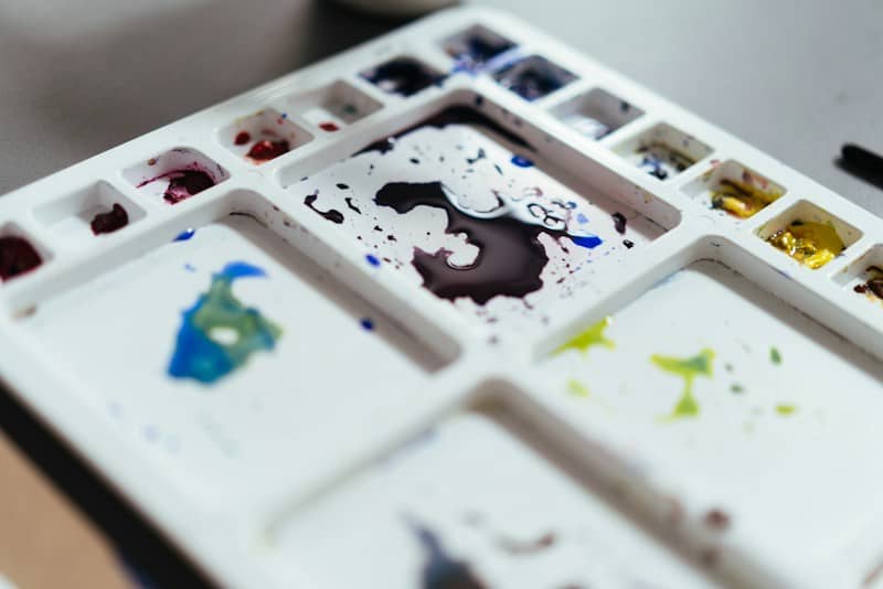 A white plastic paint palette with pools of purple, blue, and yellow watercolor