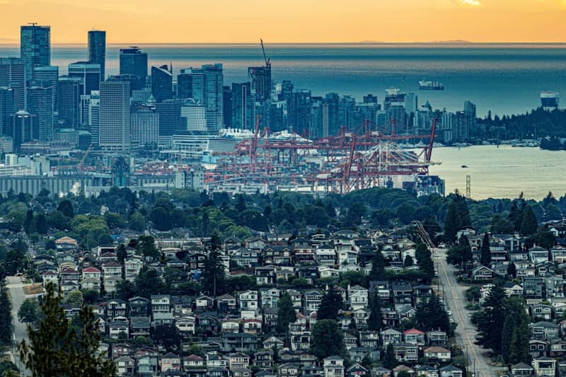 City skyline, port cranes, and residential houses at sunset.