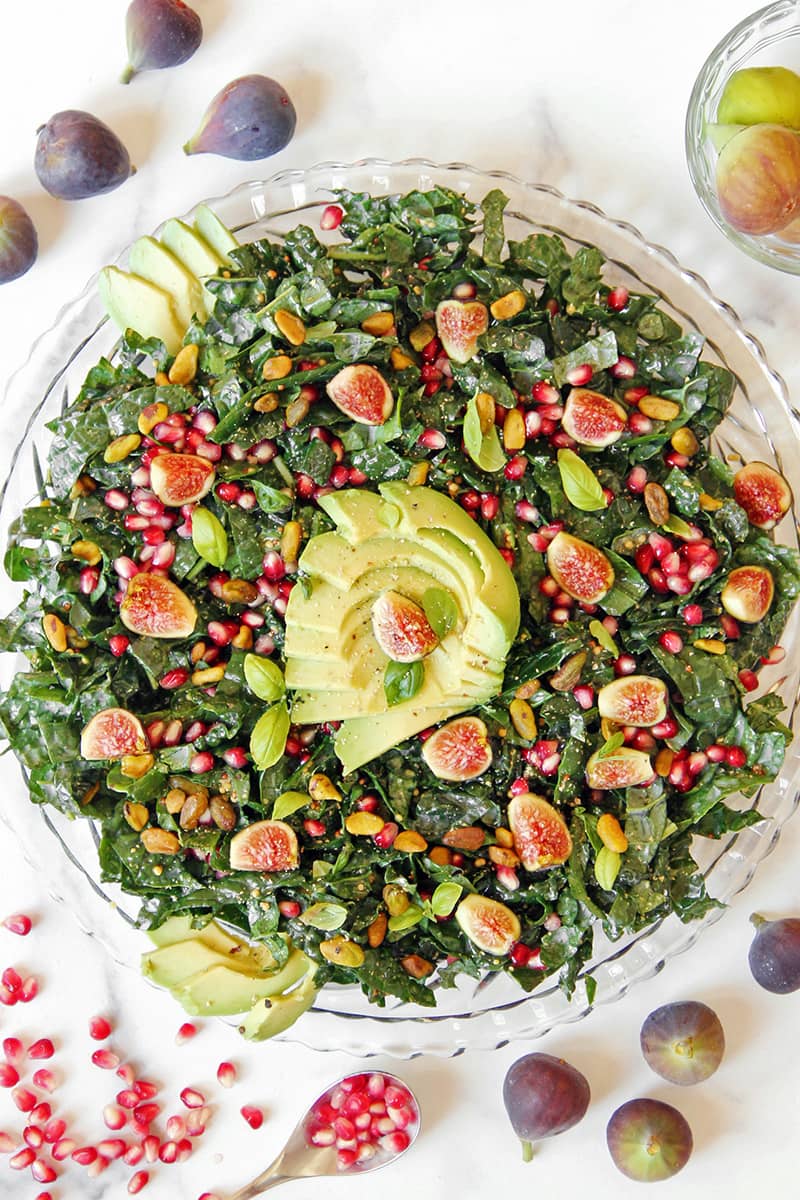 A beautiful kale salad with figs, pomegranate, and avocado, shown with fresh figs of different colors