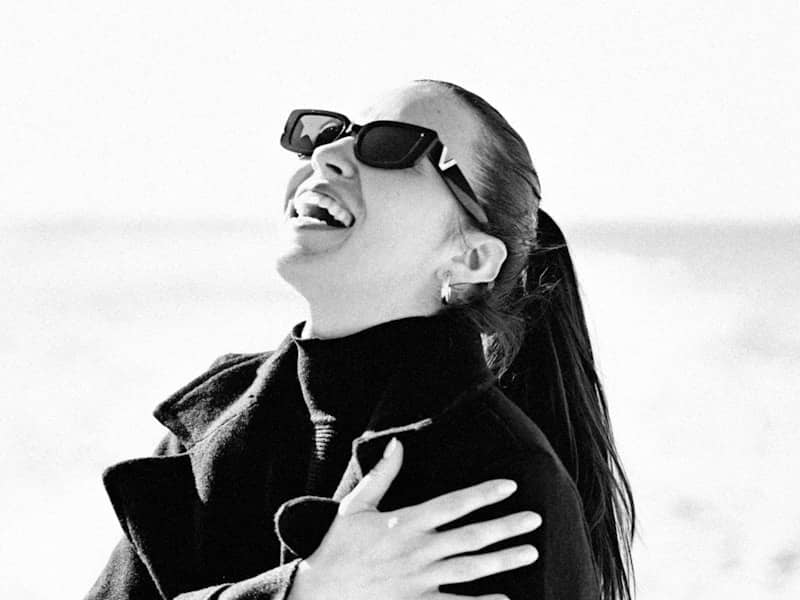A woman in sunglasses laughs with her eyes closed.