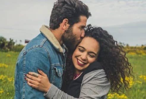 man kissing on woman's head on the green grassy field