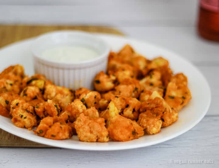 Vegan buffalo cauliflower bites on a plate, with a dipping sauce in a ramekin.