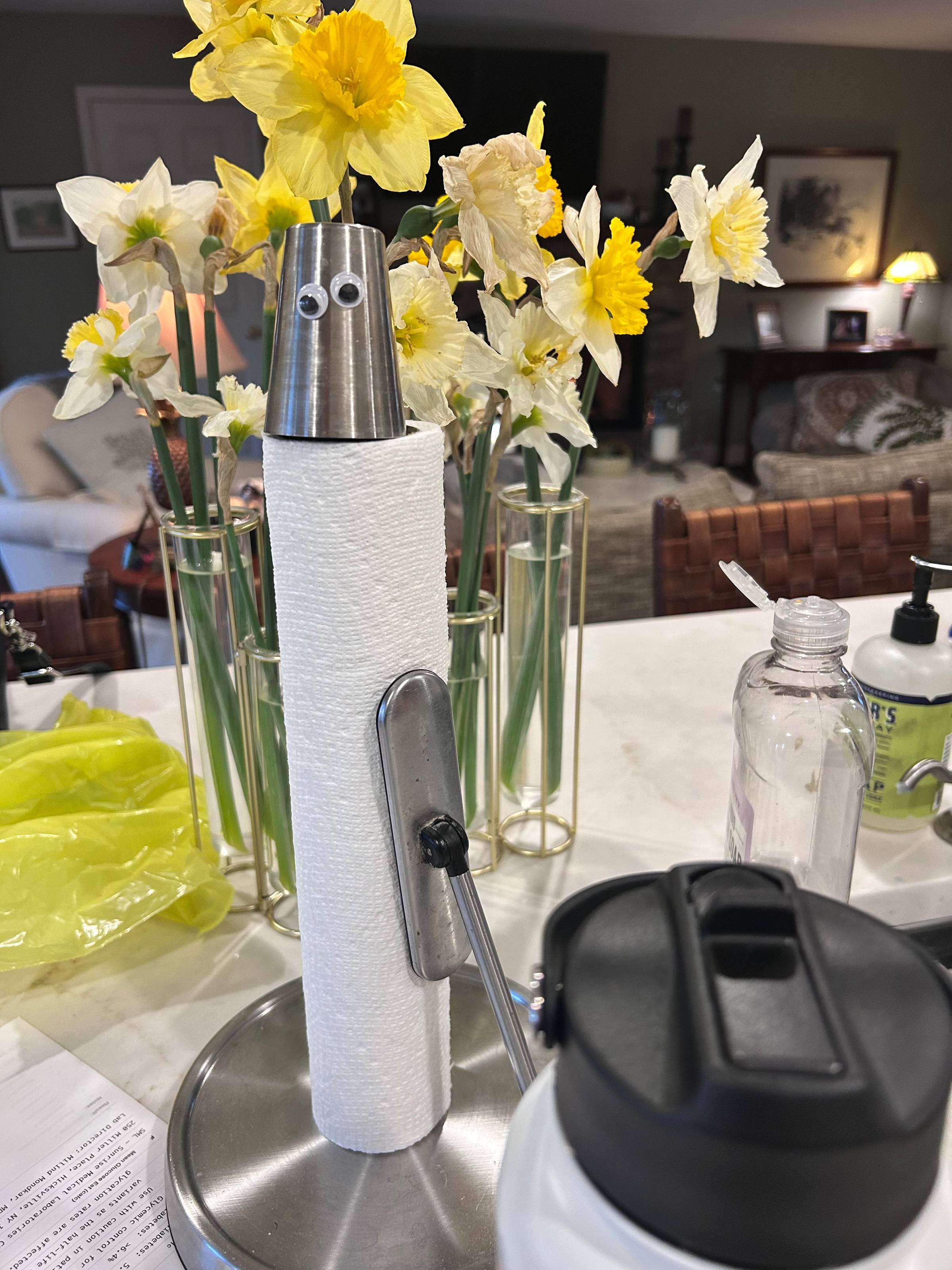 googly eyes on a paper towel holder with flowers behind