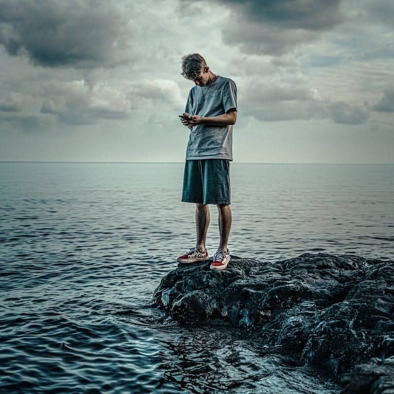 woman in white long sleeve shirt and blue skirt standing on rock in front of sea