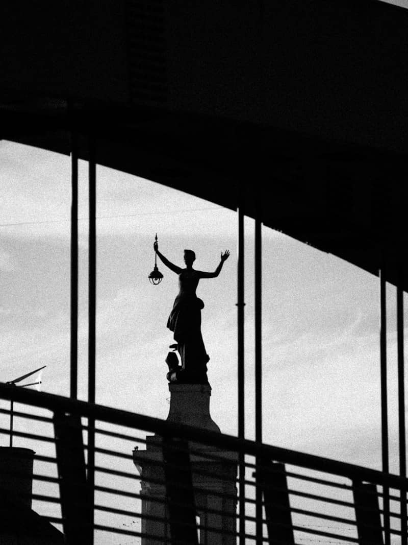 A silhouette of a statue holding a lantern against a bright sky