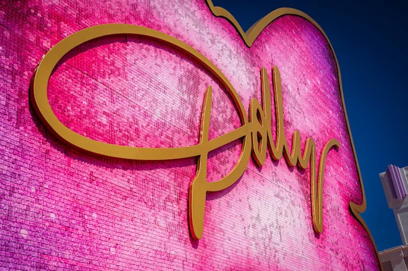 A large pink sequined heart sign with gold cursive lettering against a blue sky