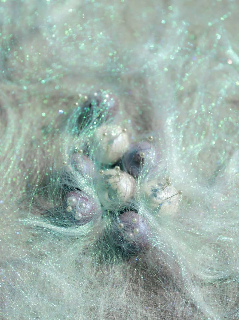 Small spheres with pearl pins nestled in iridescent mint green synthetic hair fibers