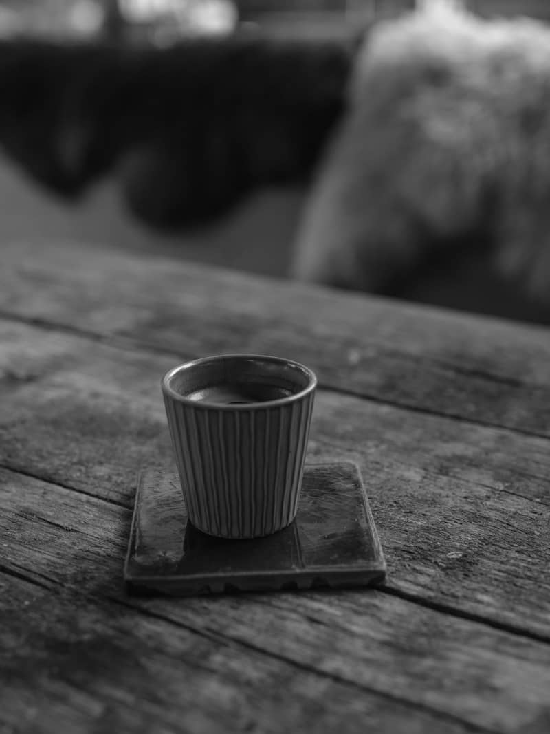A small ribbed cup on a square coaster atop a rustic wooden table