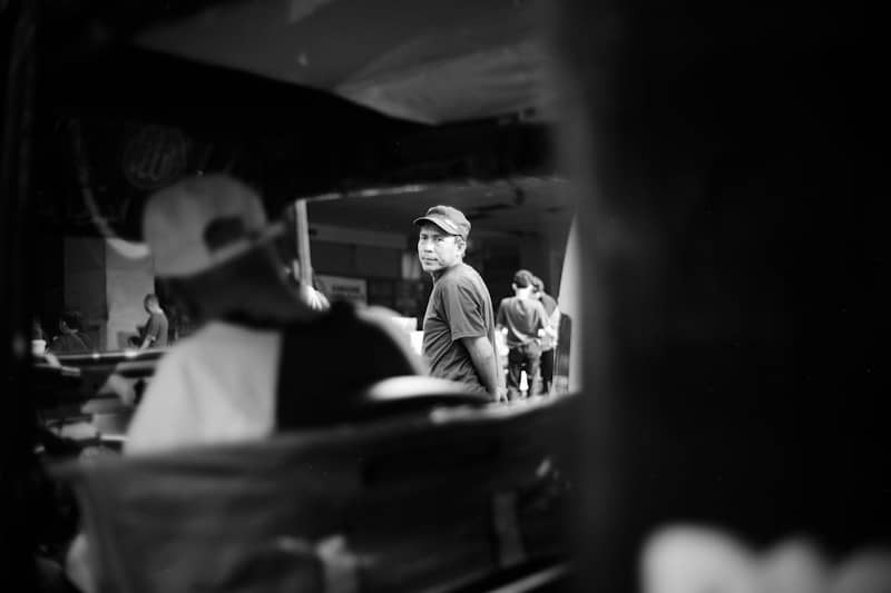 A man in a cap looking back from a street scene in black and white