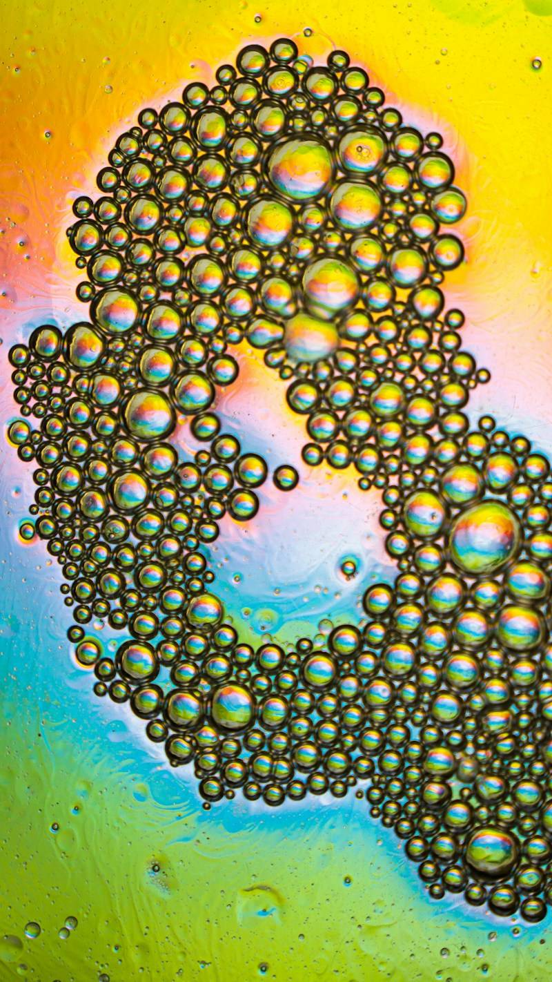 Iridescent oil bubbles in a cluster against a vibrant yellow and blue background