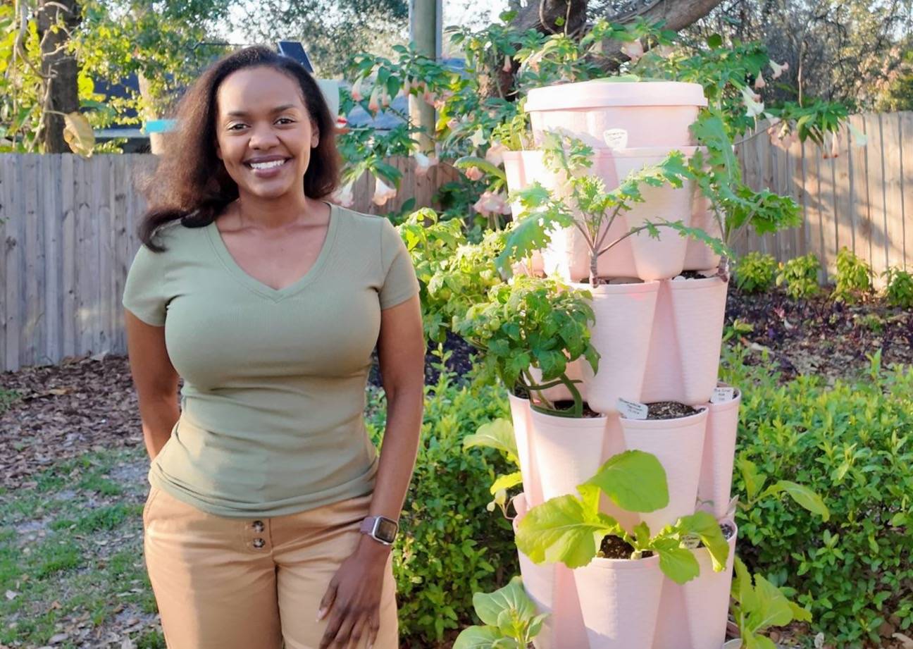Courtney smiling beside a pink GreenStalk planter filled with leafy greens in her Florida backyard garden during golden hour light.