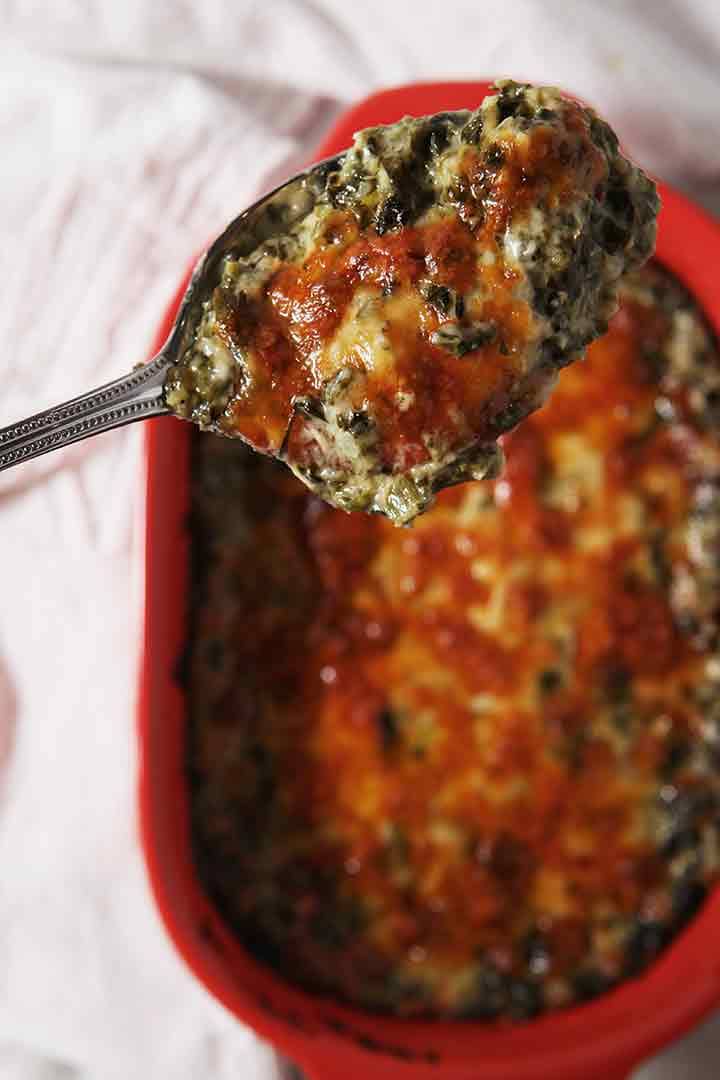 a spoon holds a scoop of creamy cheesy spinach