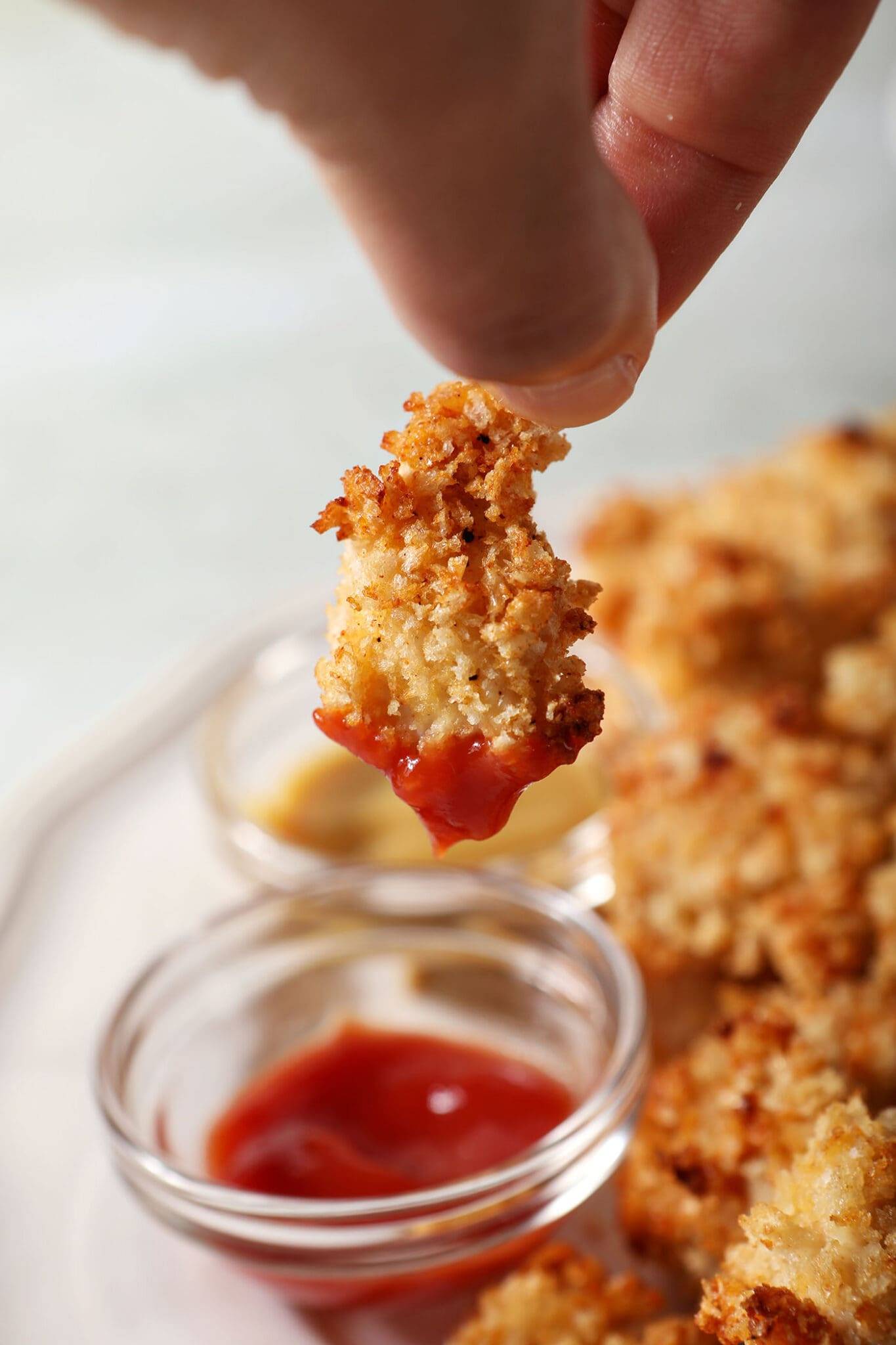 a homemade chicken nugget dips into a bowl of ketchup