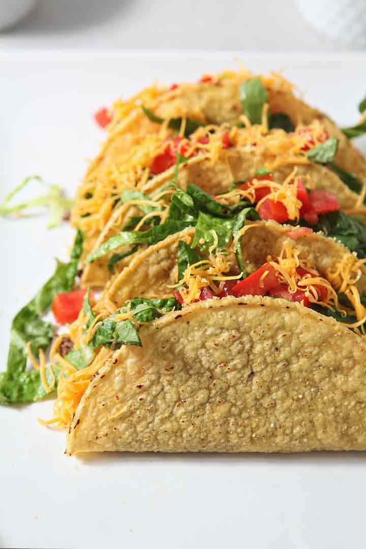 Three crunchy tacos lean on each other's side on a white platter. 