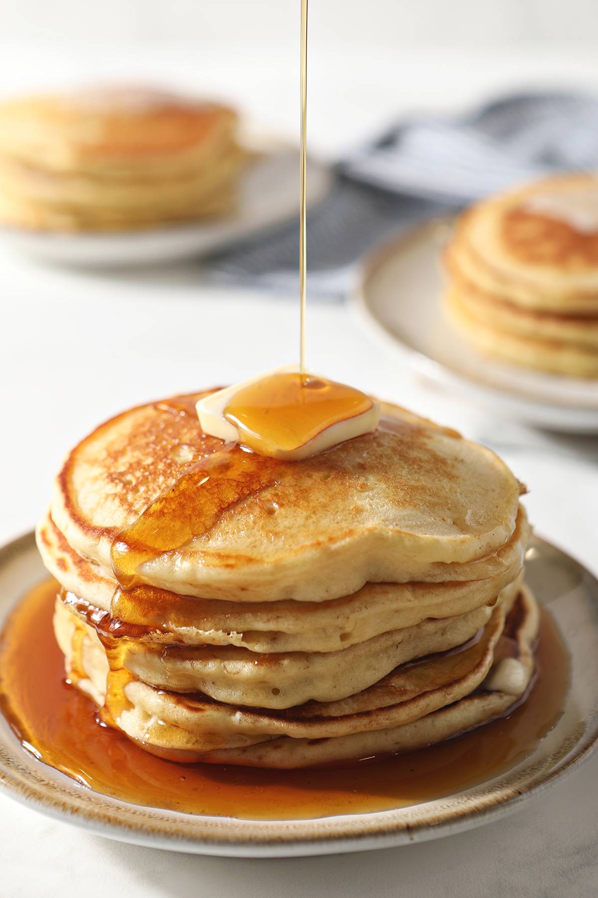 syrup drizzles onto a stack of buttery pancakes