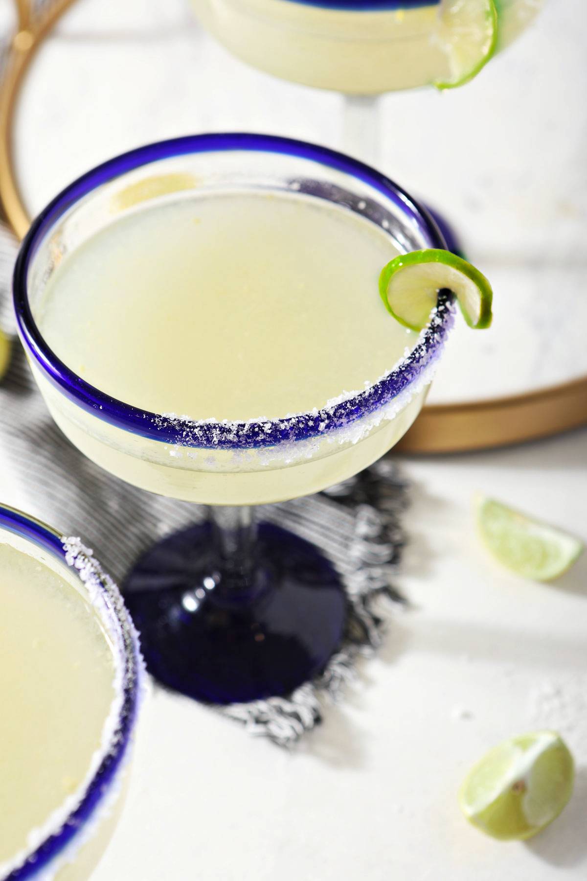 three glasses with blue rims hold margaritas on a marble surface