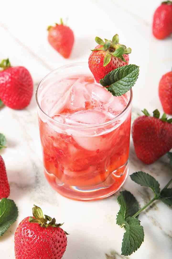 a bright red strawberry mule on marble surrounded by mint leaves and strawberries