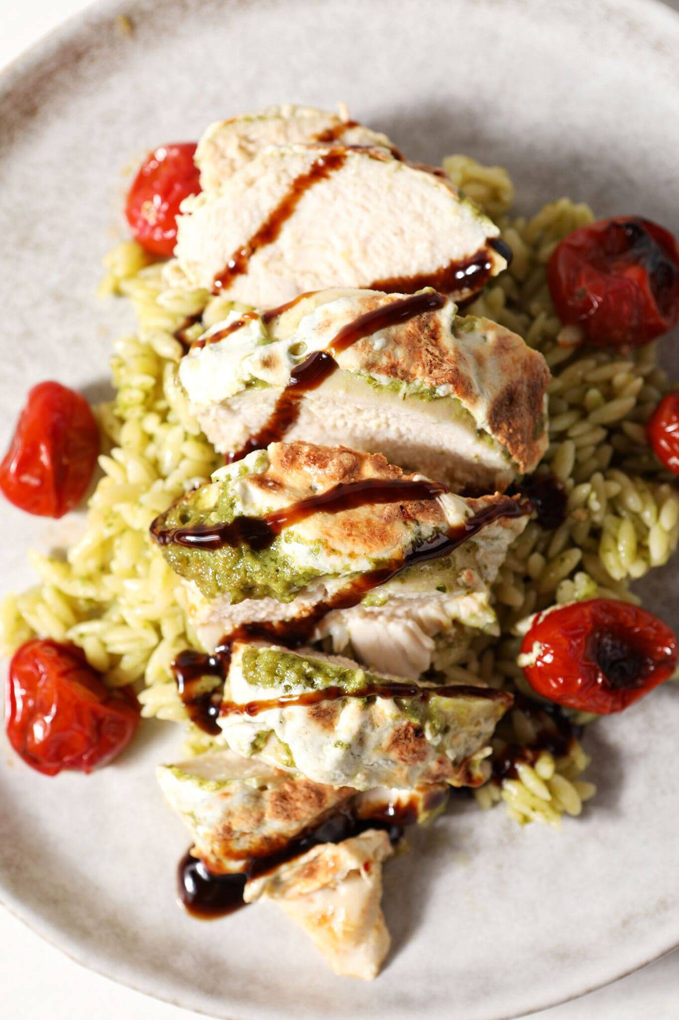 overhead of sliced caprese chicken on top of pesto orzo with roasted tomatoes