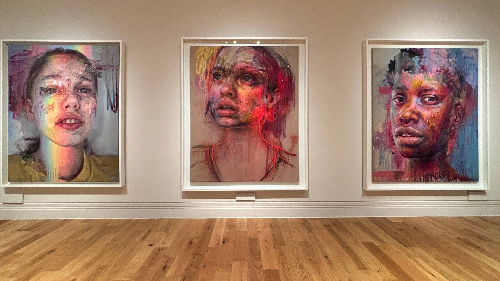 Three Jenny Saville portraits spaced across a wall in a gallery setting