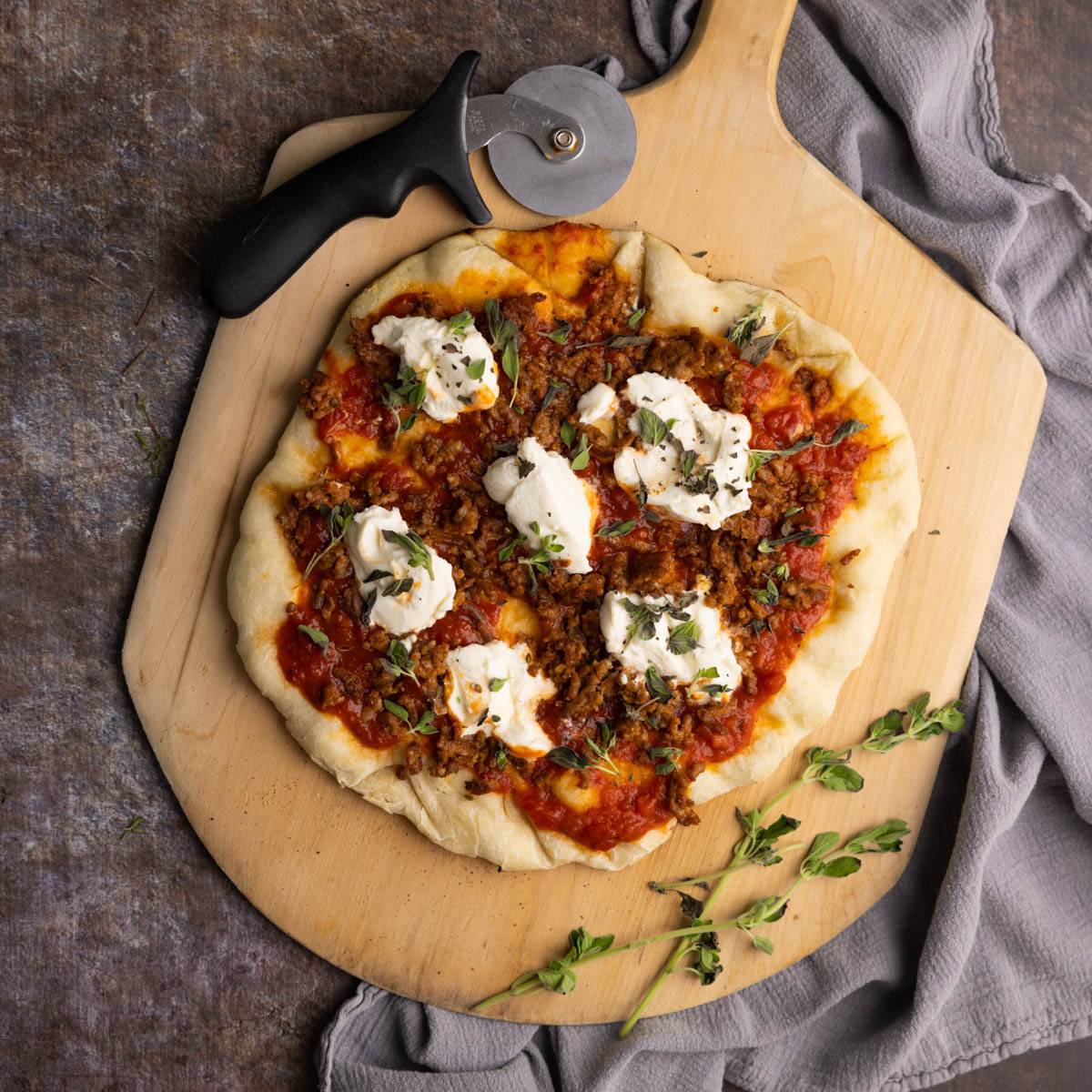 grilled pizza topped with ricotta, sausage and fresh herbs on a pizza peel.