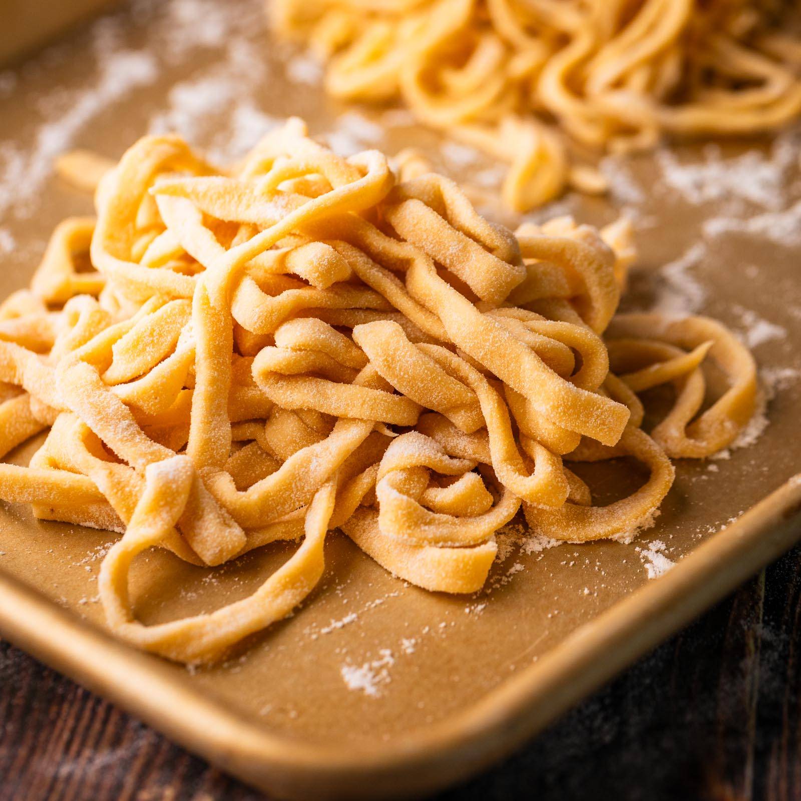 pile of fresh cut pasta on a sheet pan with flour.