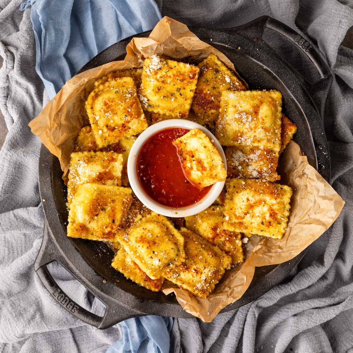 fried ravioli in a dish around a small dish of marinara sauce with a ravioli dipped in it.