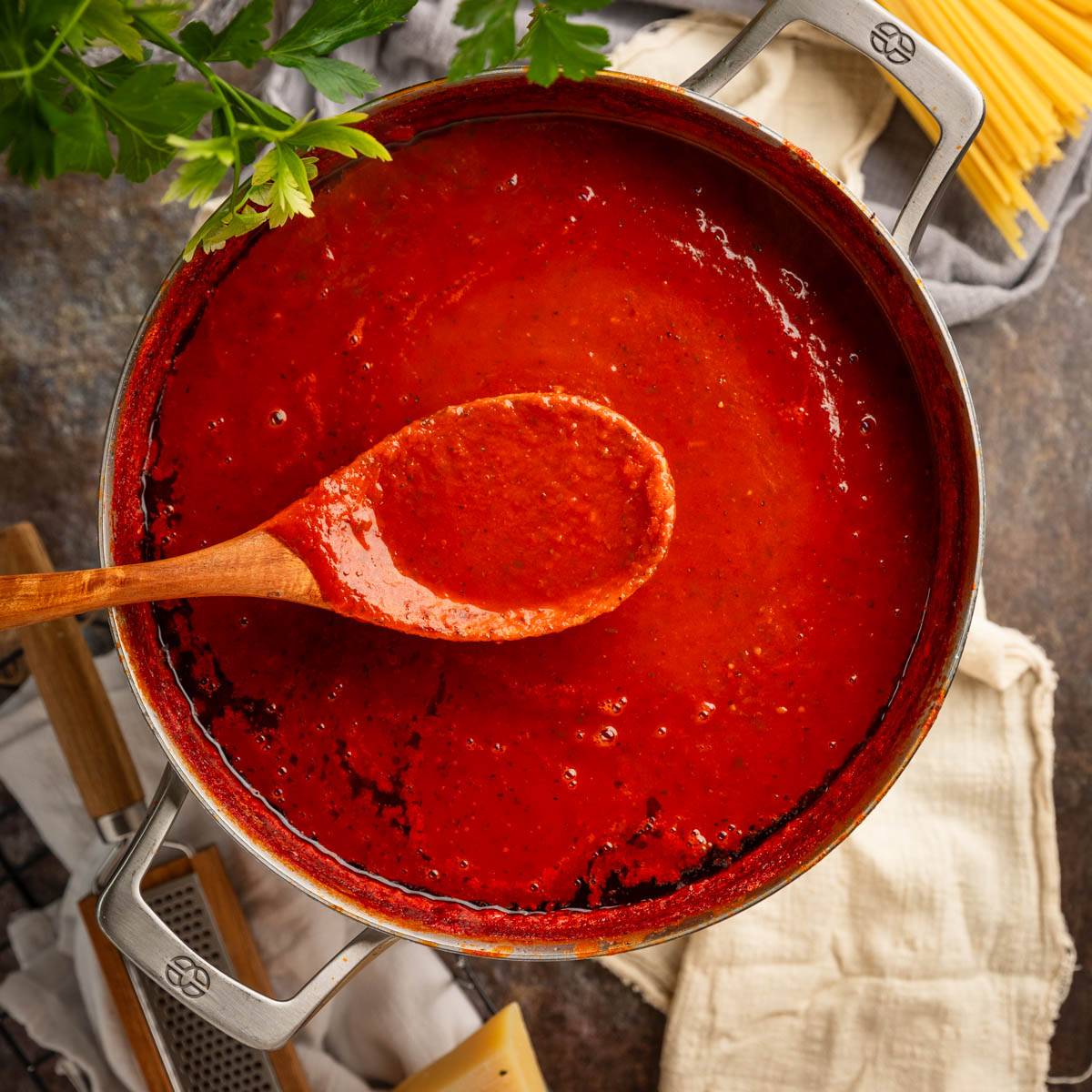 wooden spoon holding a scoop of red sauce over a pot.