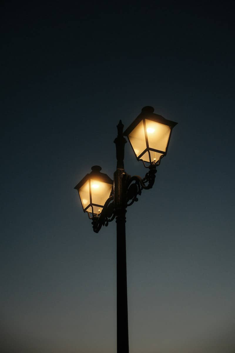 A black metal street lamp with two glowing lanterns against a dark sky