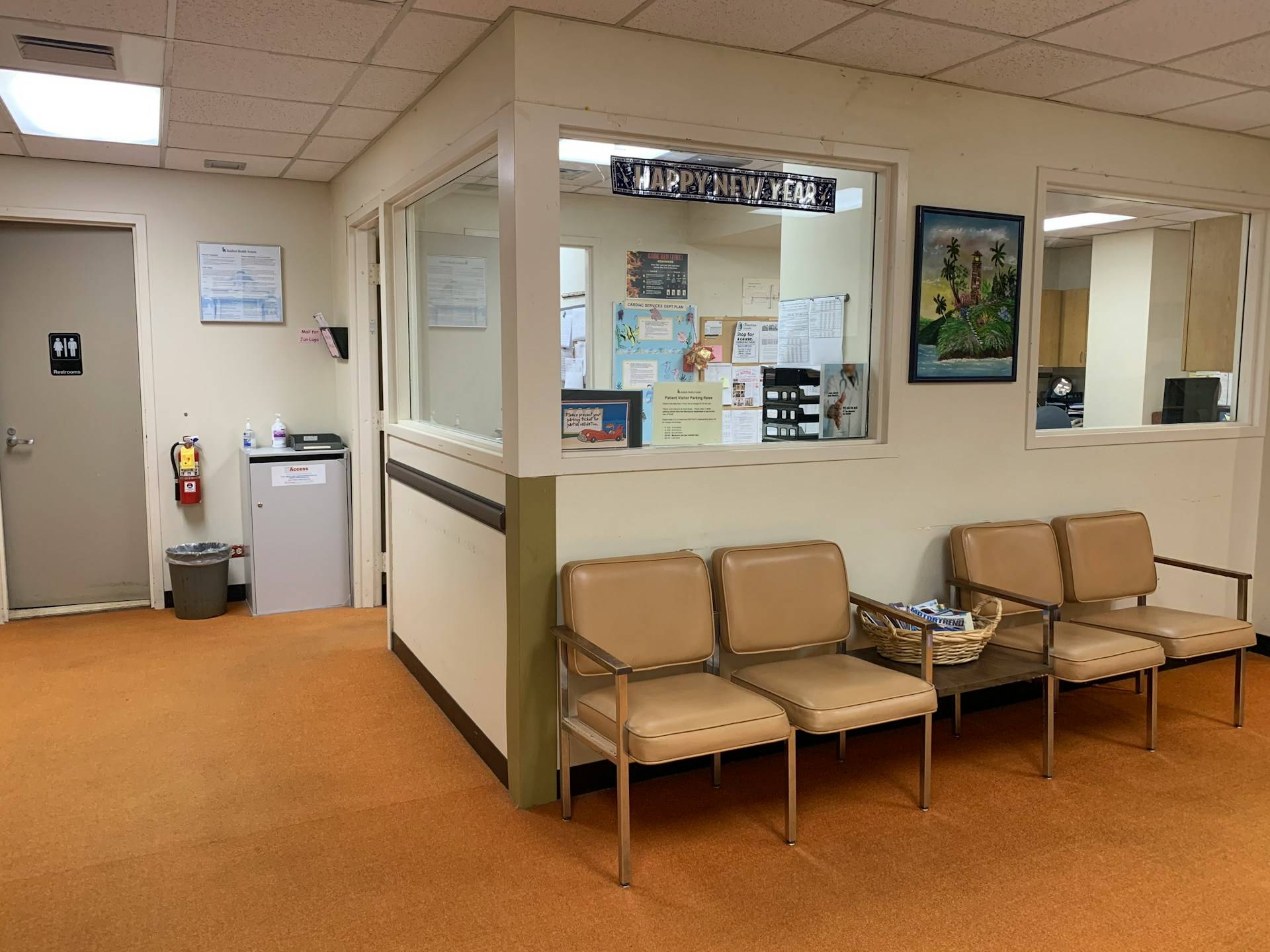 A sterile medical office waiting room captured in all its fluorescent-lit mundanity. Four tan vinyl chairs with wooden armrests line the wall beneath a large window looking into the reception area, where bulletin boards covered with forms and notices are visible. The orange-brown carpeted floor, cream-colored walls, and institutional furniture create the familiar feeling of anxious waiting—the kind of space where small talk with strangers can feel either comforting or invasive, depending on what they choose to say. 