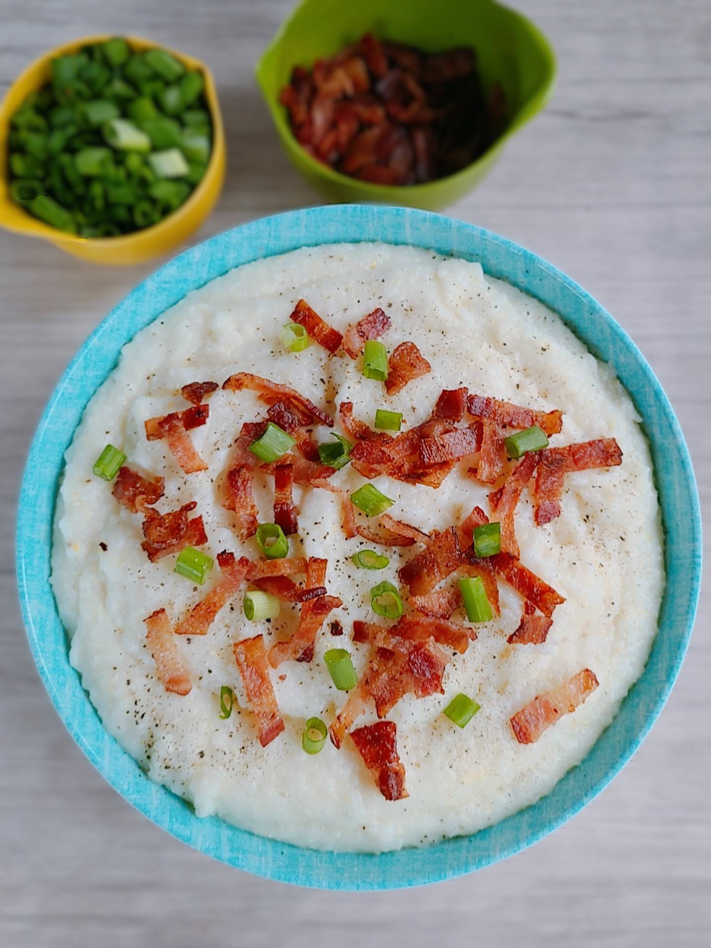 Cheesy grits with bacon and green onions in a teal bowl.
