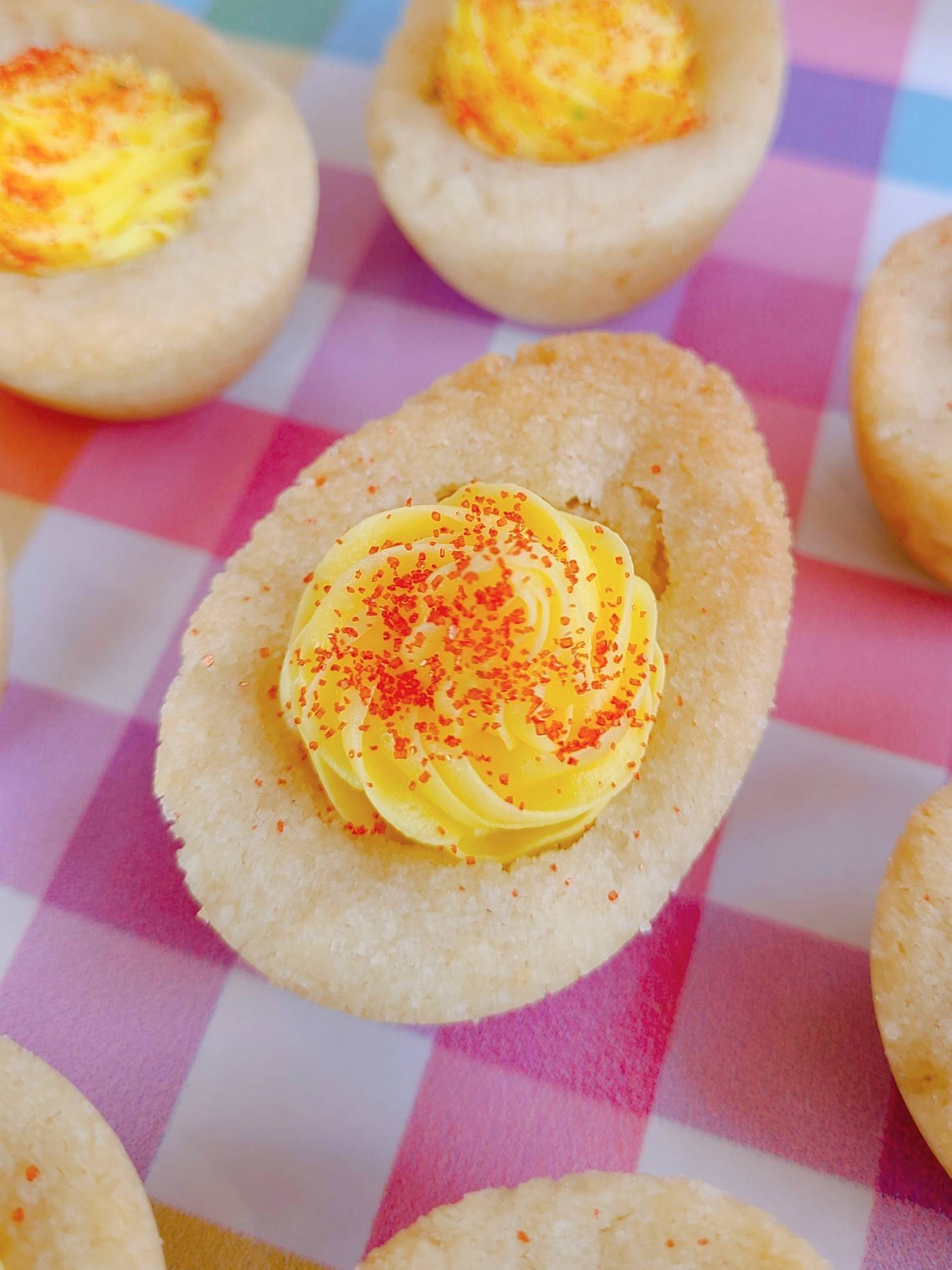Deviled Egg Sugar Cookie with frosting yolk and sanding sugar paprika on a plaid plate. 