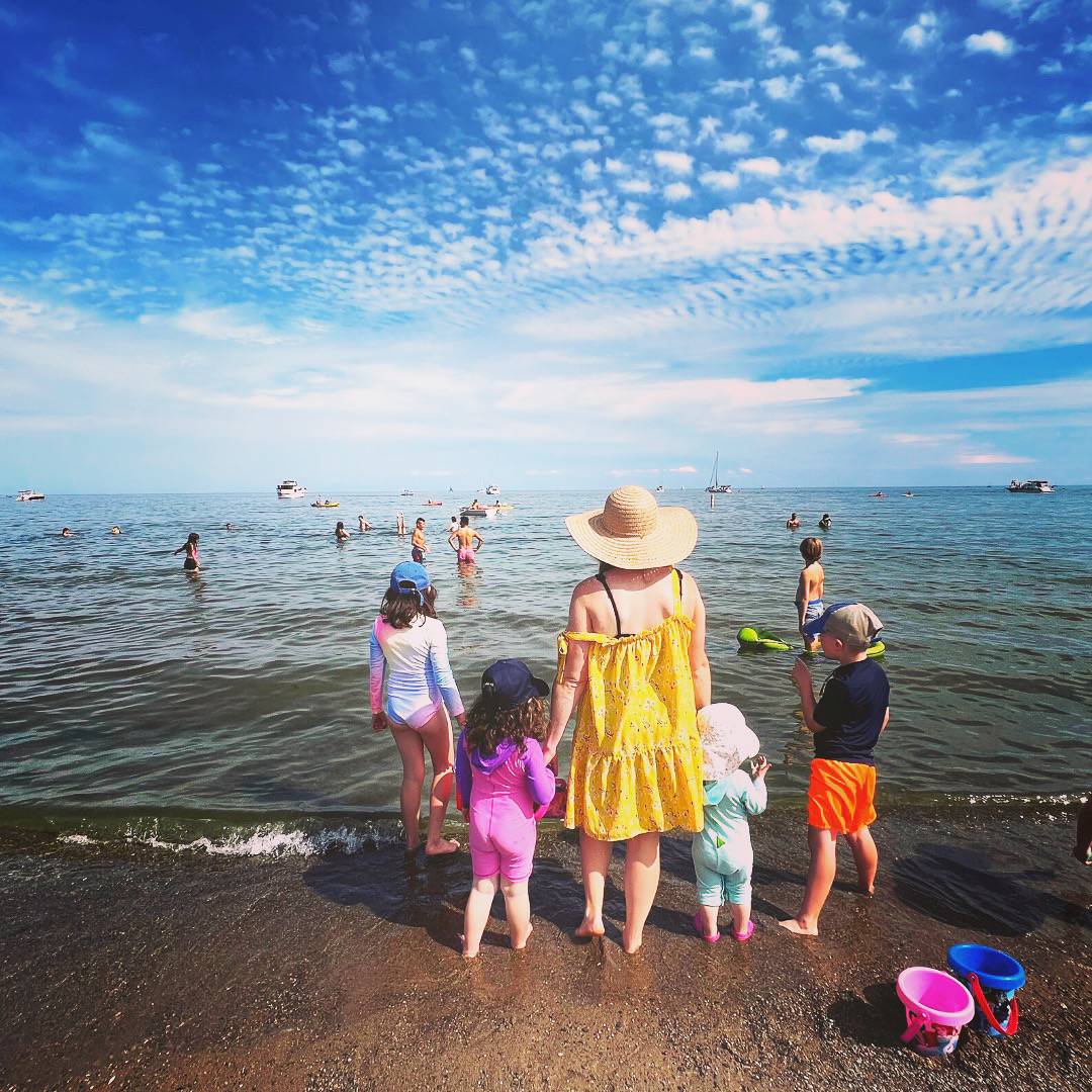 Rebecca Joy, standing on beach at water's edge with four children, facing the water, back to camera