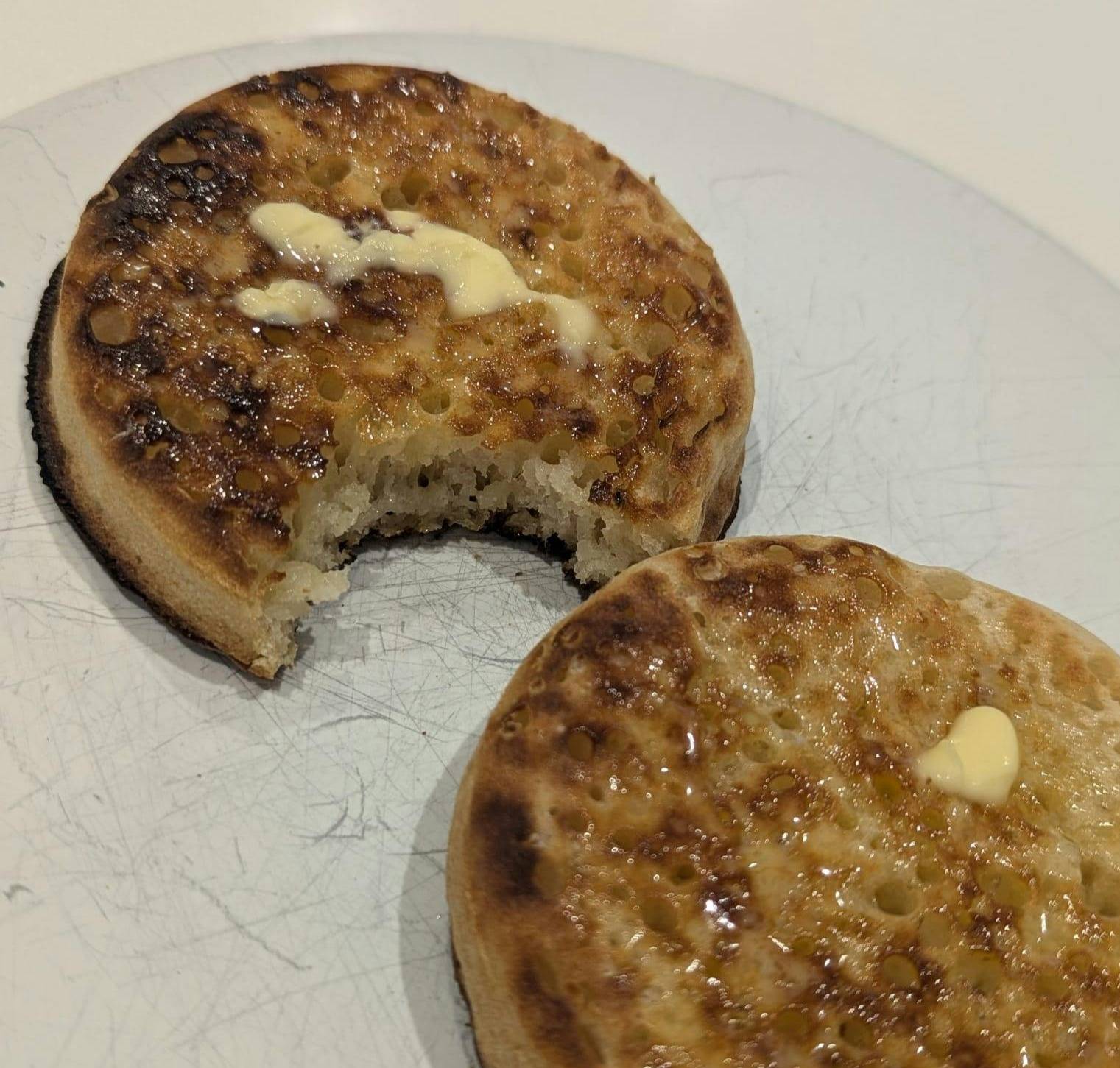 a picture of who slightly singed crumpets on a white plate. One has a bite taken out of it.