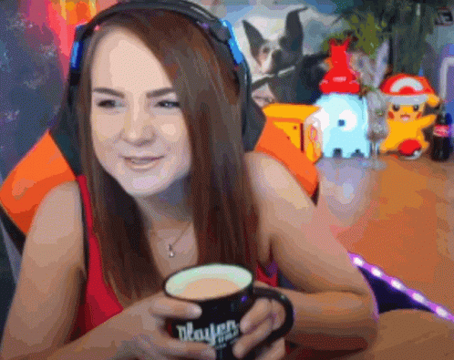Smiley woman at a wooden desk in a red top with a cup of tea that she takes a gulp from and spills down her top. She ends look exasperated.