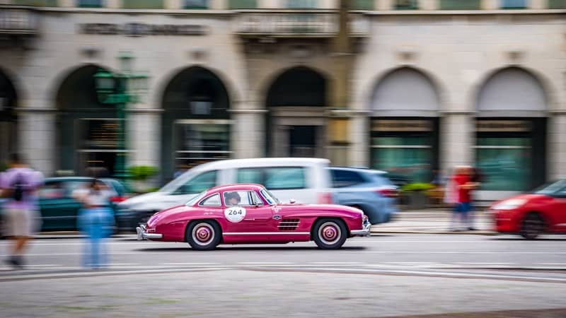 A classic pink car driving on a street.