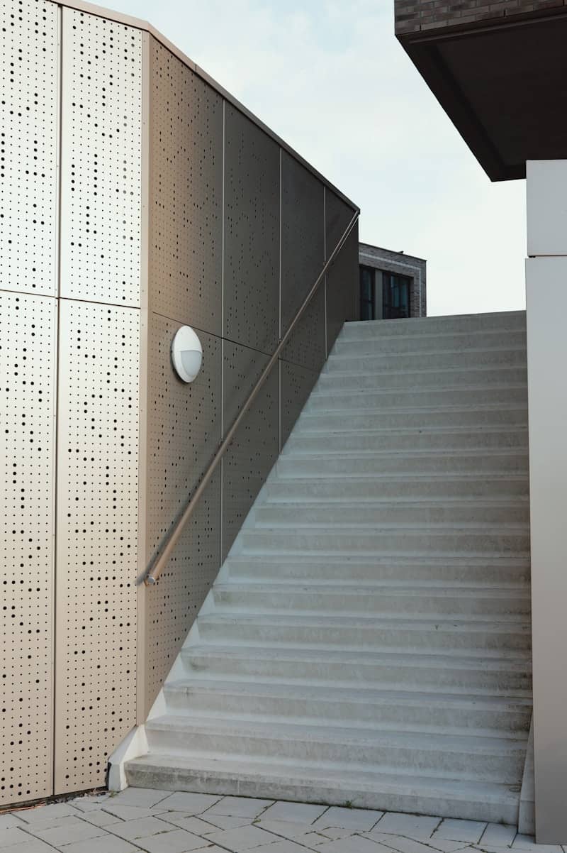Modern concrete stairs ascend beside perforated metal wall.