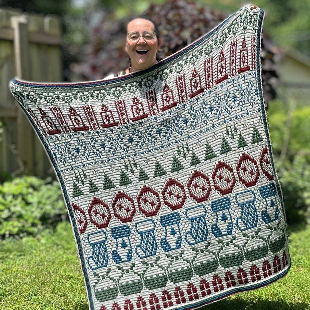 A woman holding up a Christmasy mosaic crochet blanket