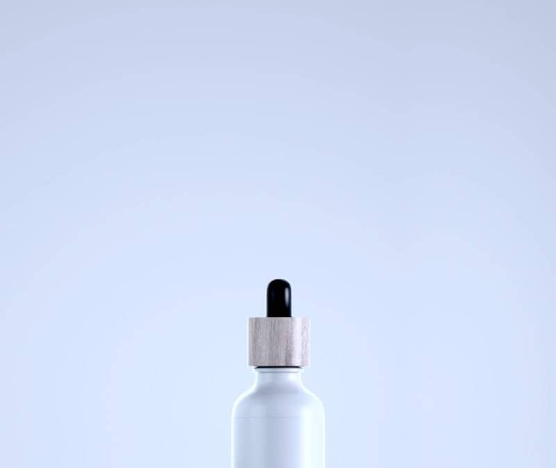 White bottle with dropper on mossy branch with flowers