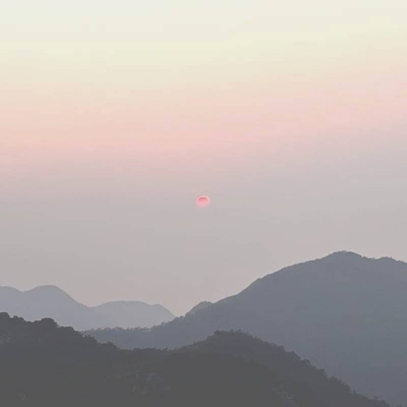 Distant sun setting over silhouetted mountain ranges.