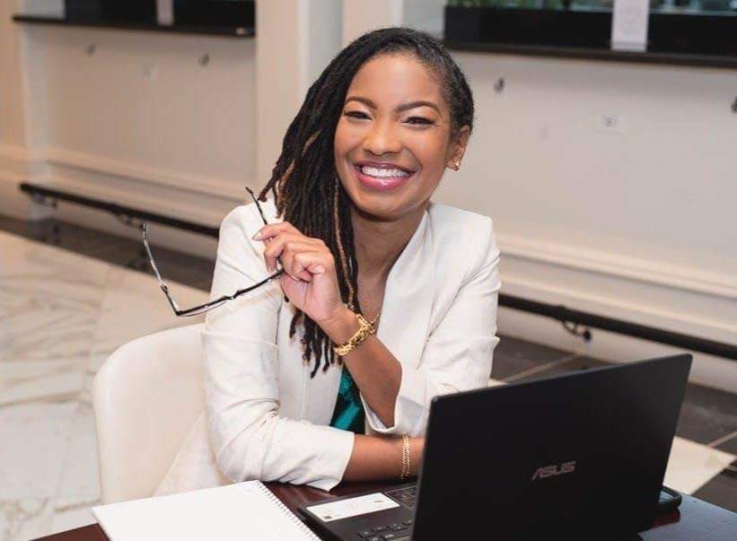 Professional Black woman sitting at laptop, holding glasses and smiling
