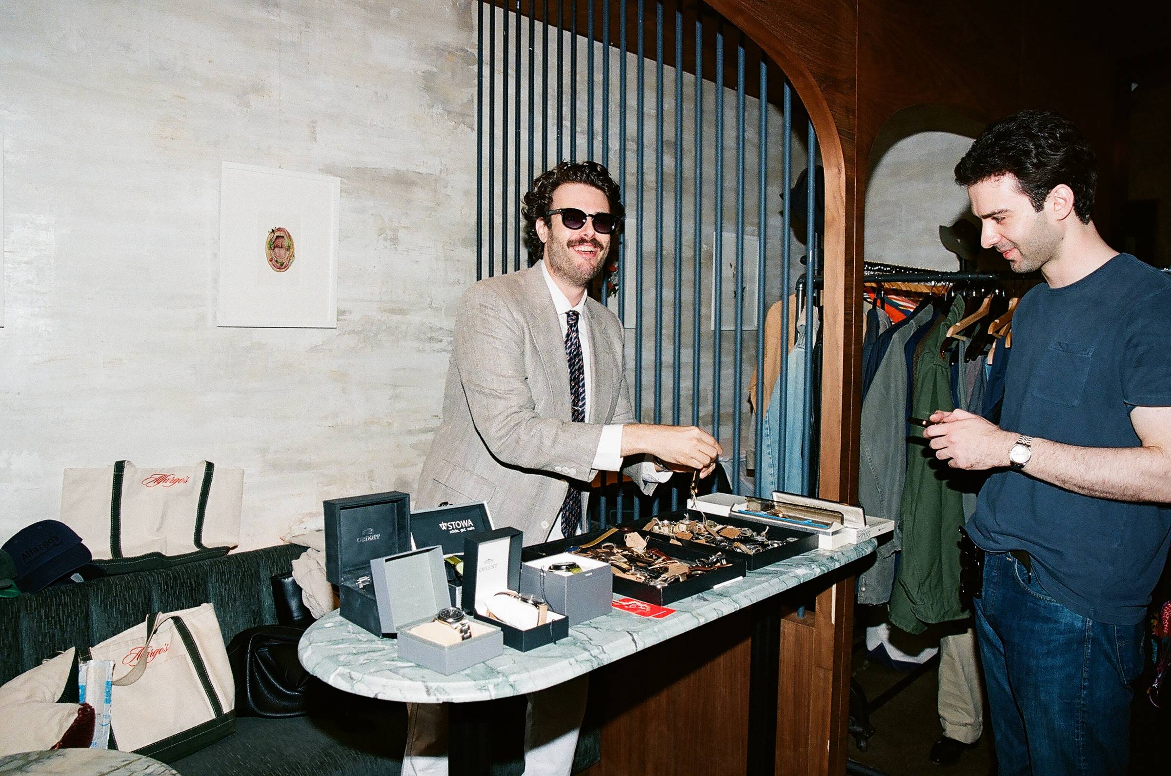 Aaron selling vintage watches from a pop-up setup, arranging timepieces and watch boxes while talking with a customer.