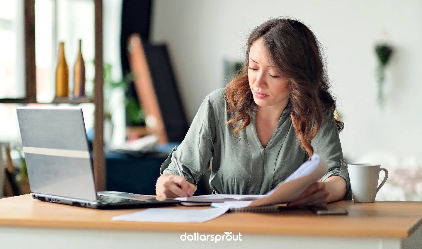 Woman working at a laptop with paperwork and coffee, representing the middle-class creator economy.